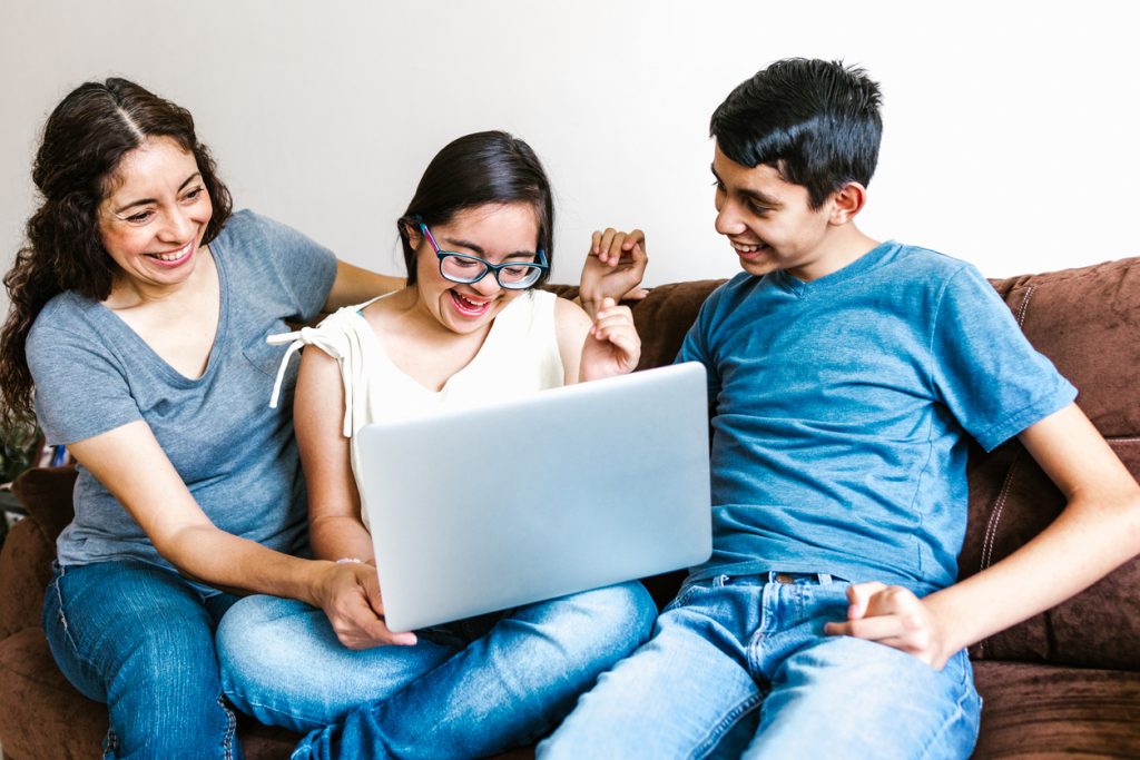 a  woman, girl and boy sitting on a sofa smiling while looking at a notebook computer. 
