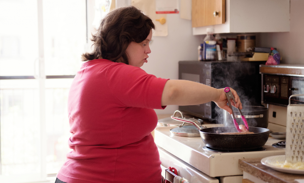 A disabled woman holding tongs cooking a dish in a pan.